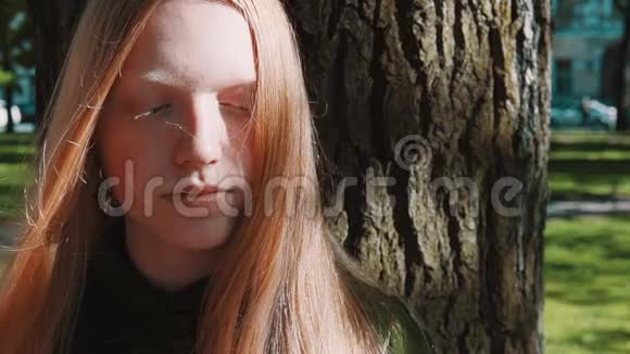 一个长头发的姜姑娘站在公园树下视频的预览图