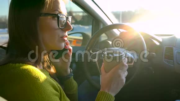 戴眼镜的女人在智能手机上说话在车里喝咖啡视频的预览图