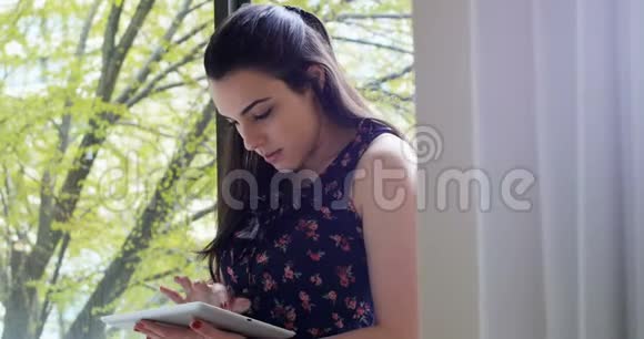 漂亮的女人在4k窗口附近使用数码平板电脑视频的预览图