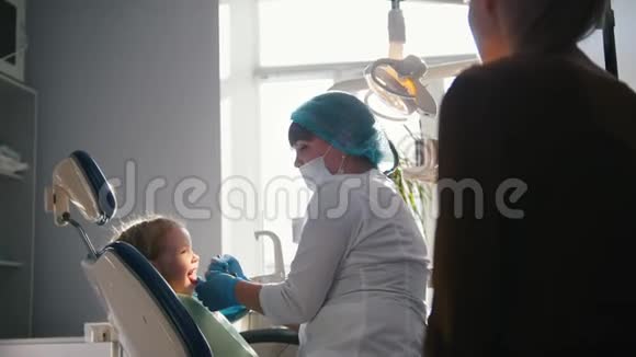 带着妈妈坐在牙医椅上的小女孩孩子在玩视频的预览图