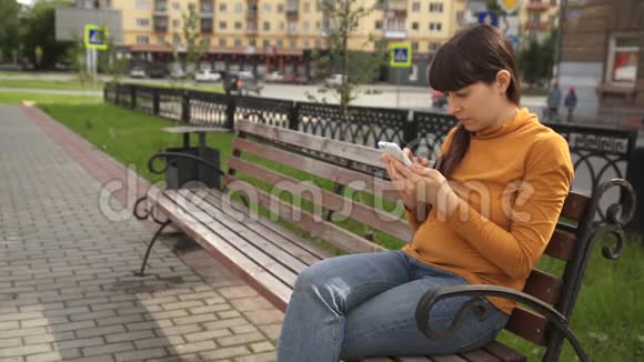 坐在路边长凳上打电话的年轻女子视频的预览图
