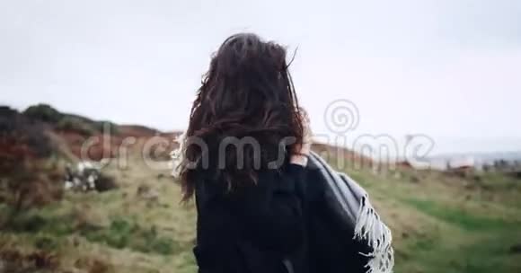 一位戴着围巾的女士在镜头前调情走在海边的一片山地上慢动作4k视频的预览图