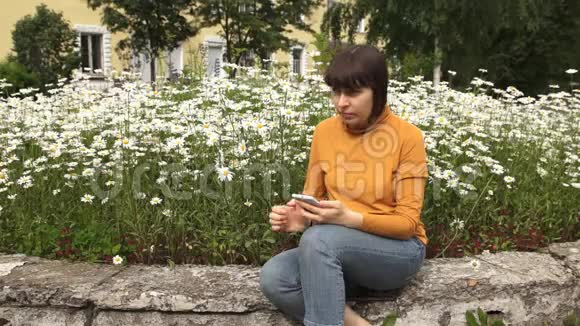一个穿着黄色高领毛衣的黑发女人用电话坐在卡莫米尔斯旁边视频的预览图