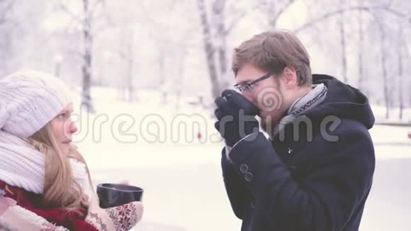 美丽的女人和留着胡子的男人在冬天的公园里聊天喝着杯子里的热可可4K侧视图视频的预览图