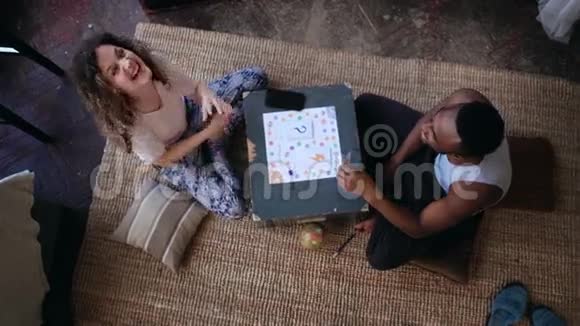 多种族夫妇穿着睡衣坐在地板上玩棋盘游戏男人和女人笑着给猴子看视频的预览图