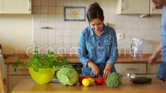 漂亮的年轻家庭主妇站在厨房的桌子上切蔬菜她丈夫走过来拥抱他亲吻他视频的预览图