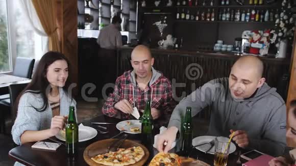 在餐厅里吃比萨饼和喝啤酒很有趣两个男人和两个女孩在披萨店视频的预览图