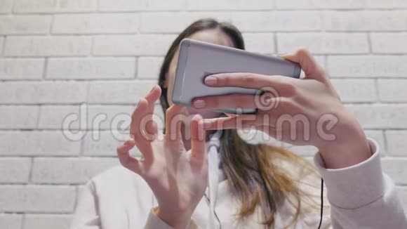 美丽的黑发女人看着一个系列耳机在手机上的砖墙背景视频的预览图
