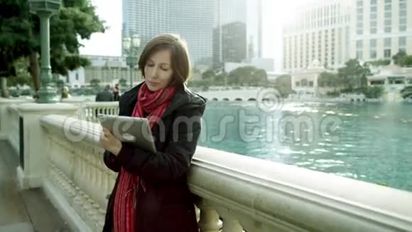 年轻的美女站在喷泉旁边手里拿着平板电脑视频的预览图