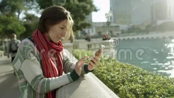 美丽的女人正在喷泉前使用智能手机视频的预览图