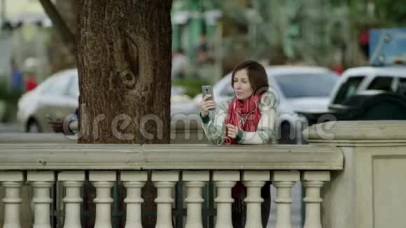 年轻漂亮的女人正在树旁的人行道上视频聊天视频的预览图