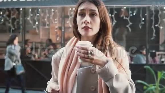 漂亮的女孩拿着一杯咖啡站在橱窗前梦想买东西叹息慢动作视频的预览图
