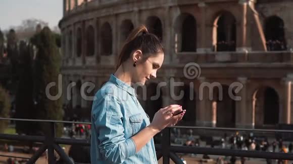 年轻女子在意大利罗马的竞技场背景下使用她的智能手机看上去有点悲伤慢动作视频的预览图