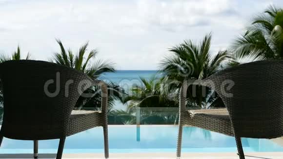 全高清在靠近海滩的游泳池前用椰子树和海景放大两张休闲度假椅视频的预览图