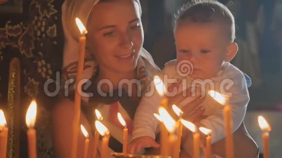 小儿子的年轻母亲在教堂里观察着燃烧的蜡烛视频的预览图