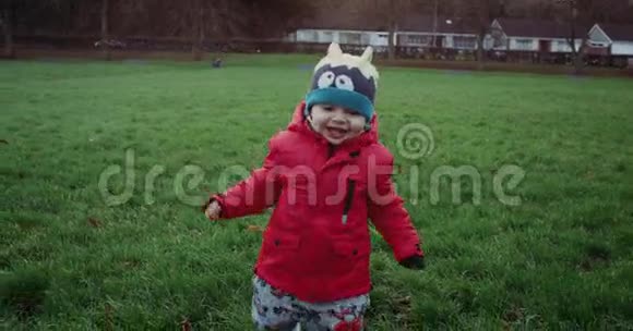 快乐的小男孩穿着红色夹克在公园里微笑着跑步孩子在绿草上奔跑慢动作4k视频的预览图