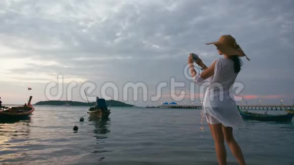 美丽的女人在天堂海滩用智能手机拍照视频的预览图