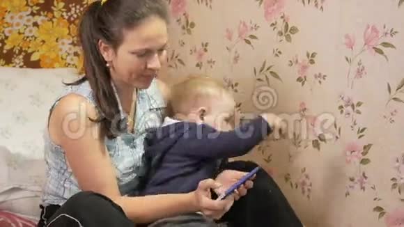 年轻女子带着儿子坐在家里的沙发上拿着手机孩子想摆脱拥抱视频的预览图