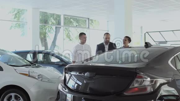 售货员向汽车经销店里的一对年轻夫妇讲述汽车的事视频的预览图