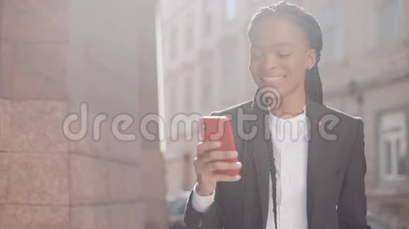 时尚的非洲商业女性使用智能手机在商业中心附近的街道上行走黑色时尚可怕的家伙非洲裔视频的预览图
