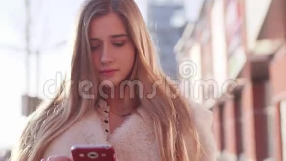 阳光明媚的早晨一位年轻漂亮的金发女郎站在一栋现代化建筑附近用手机滚动着她的食物视频的预览图