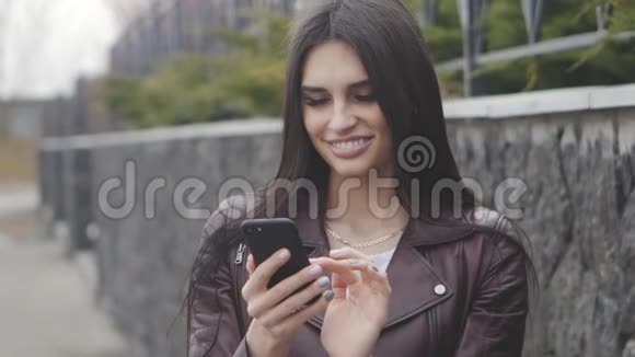 一个黑发女人在街上微笑并使用智能手机的肖像视频的预览图