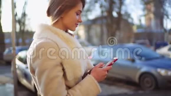 年轻漂亮的金发女郎走在街上在许多汽车驶过的时候她在智能手机上发短信她是视频的预览图