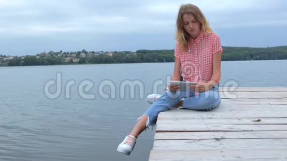 女人在平板电脑边慢吞吞地坐在湖边视频的预览图