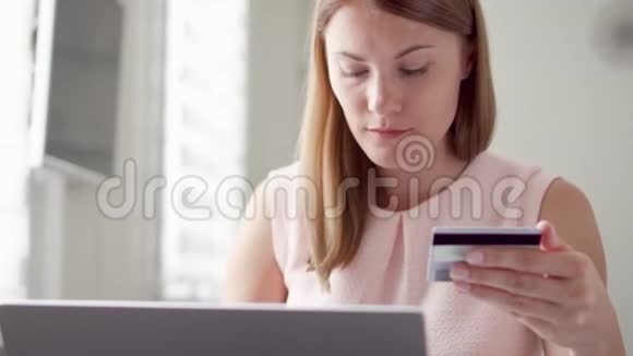 年轻漂亮的女人坐在家里用笔记本电脑上的信用卡在线购物网上消费主义视频的预览图