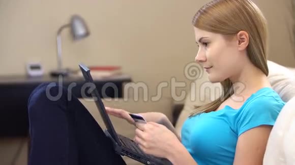美丽的年轻女子坐在沙发上手提电脑用信用卡在线购物视频的预览图