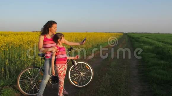 女人和一个孩子在大自然中做自拍一个快乐的母亲和她的女儿在农村被拍照自行车视频的预览图