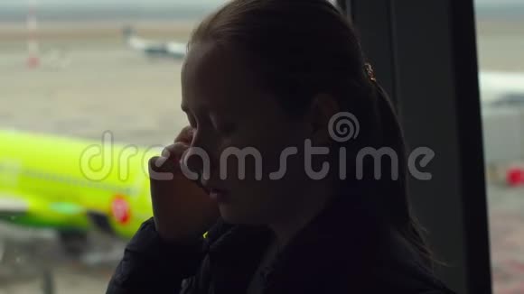 女青年在机场的一个大窗户前用手机说话视频的预览图