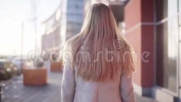 年轻漂亮的金发女郎对着镜头转了两圈带着美丽的微笑走在一条现代的风街旁视频的预览图
