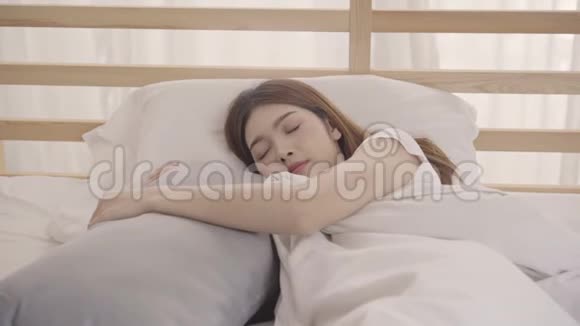 美丽迷人的年轻亚洲女人醒来微笑着伸展她的手臂在她的床上在卧室视频的预览图