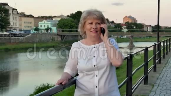 傍晚时分在海滨老城区河桥附近一位老年妇女在智能手机上聊天视频的预览图