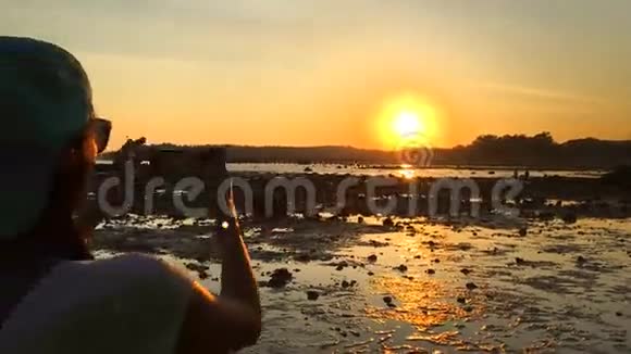 女孩用她的智能手机在海滩上拍摄惊人的日落高清慢速运动泰国视频的预览图