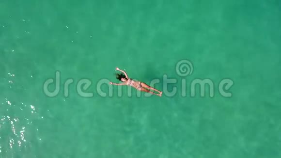 美丽的年轻女子游泳躺在清澈的海面上高清空中慢动作飞走射击视频的预览图