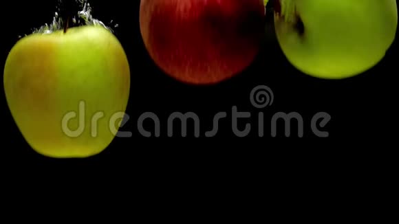 黄色红色和绿色的苹果落入黑色背景的透明水中视频的预览图