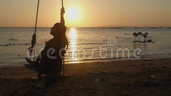美丽的年轻女子在令人惊叹的夕阳下摆动在海滩上有镜头耀斑效应慢慢慢慢视频的预览图