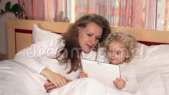妈妈带着小女孩在床上看着数码平板电脑上的东西视频的预览图