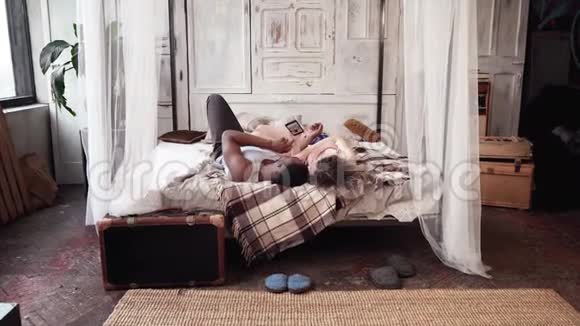 多种族夫妇躺在床上使用智能手机的后视镜非洲男人和欧洲女人看起来像照片视频的预览图