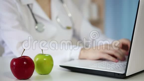 女医生在笔记本电脑键盘上打字吃着苹果健康的生活方式视频的预览图
