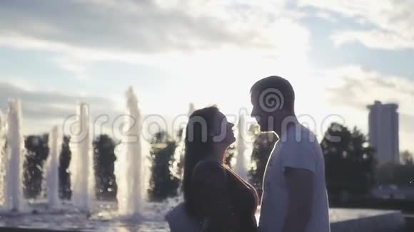 一对相爱的男人和女孩在日落背景下在喷泉附近接吻高清1920x1080慢动作视频的预览图