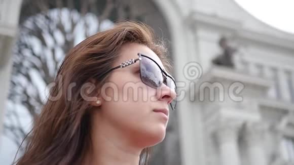 戴着太阳镜的女孩在一座美丽的建筑的背景下眺望远处高清1920x1080慢慢视频的预览图