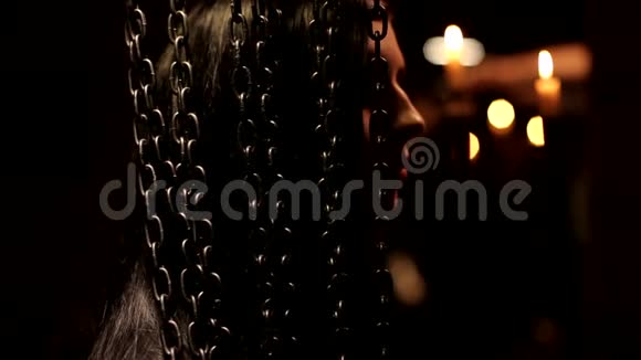 温暖的烛光黑色神秘的背景拍摄黑发美丽的年轻女子站在链帘后黑色的迈斯特视频的预览图