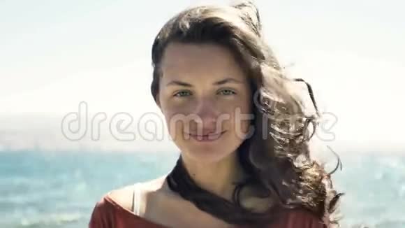 年轻女子微笑着头发美丽站在风中对着大海看着镜头视频的预览图
