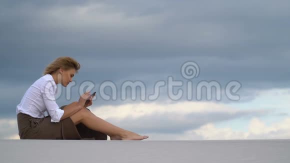 一个女孩坐在沙漠里的沙滩上打电话视频的预览图