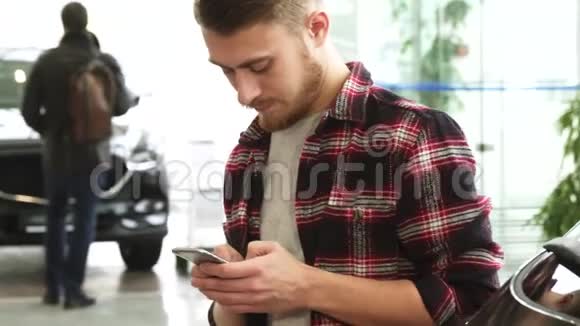 年轻的胡子男在汽车经销店用他的智能手机视频的预览图