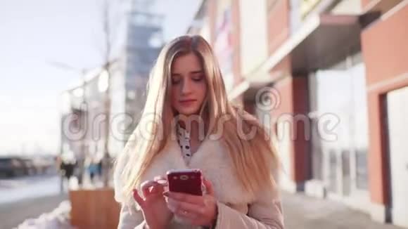 年轻漂亮的女士她的头发松松的走过市中心的现代建筑同时使用她的移动应用程序视频的预览图