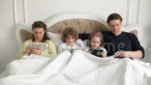 有孩子的年轻夫妇躺在床上手里拿着电子小玩意互相交谈父母视频的预览图
